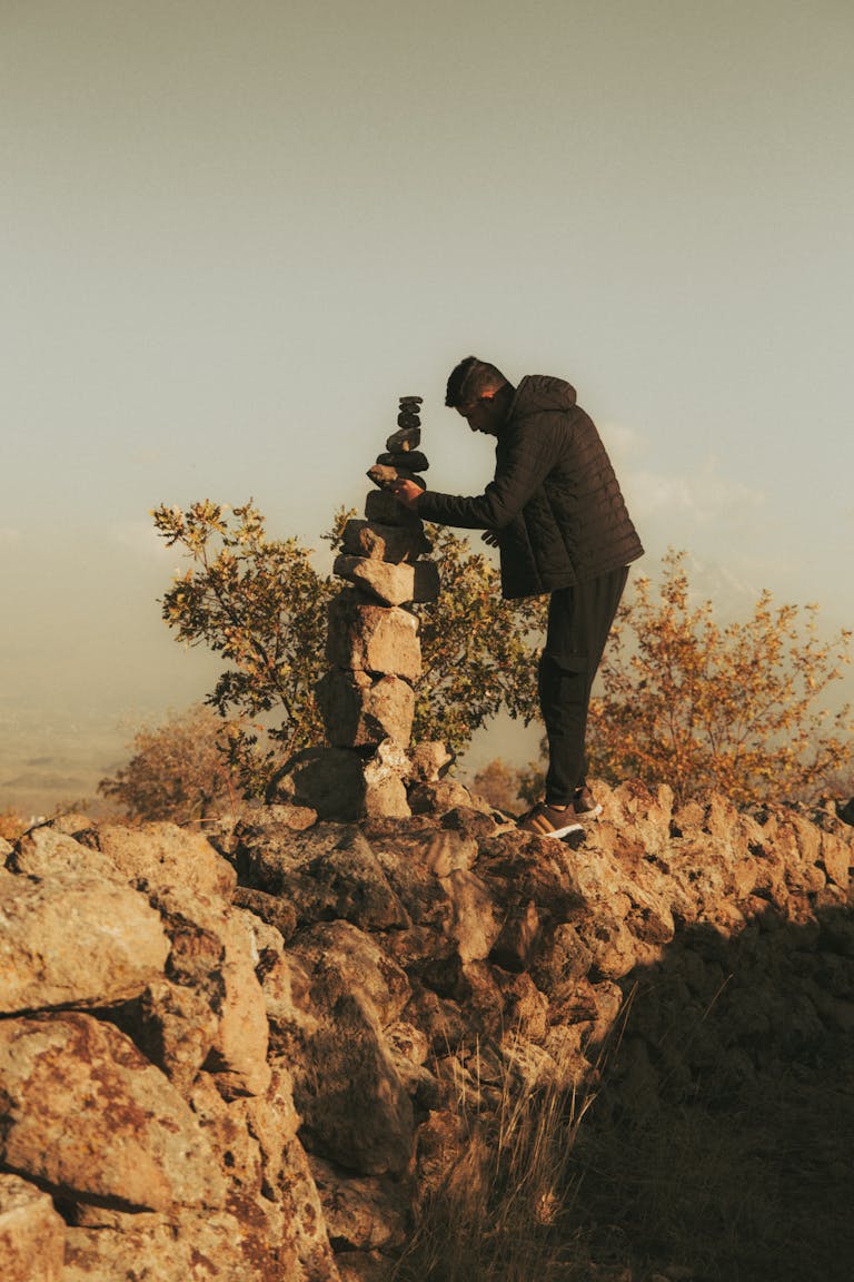 A man building a stone cairn in İncesu, Kayseri, Türkiye during sunset.